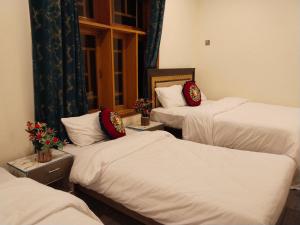 three beds in a room with white sheets and red pillows at Hunza Ray's guest house in Dargai +1 photo