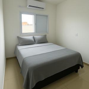 een bed in een witte kamer met een raam bij Apto Novo com Ar e Wi-Fi Perto da UFU Monte Carmelo in Monte Carmelo
