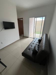 een zwarte leren bank in een woonkamer met een televisie bij Apto Novo com Ar e Wi-Fi Perto da UFU Monte Carmelo in Monte Carmelo +16 foto's