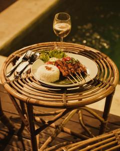 Una mesa con un plato de comida y una copa de vino. en Coral Drift Resort & Villas Gili Air, en Gili Air
