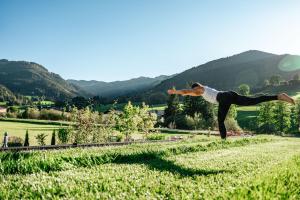 a woman doing a handstand in a field at Wellness und Brunch Hotel MorgenZeit beheizter Naturteich Genuss Frühstück bis 13 Uhr Hochkönig Sommercard in Maria Alm am Steinernen Meer