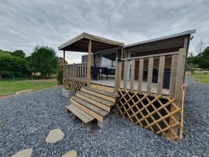 a small cabin with a wooden staircase and a porch at Belle location face à l'étang in Landouzy-la-Cour