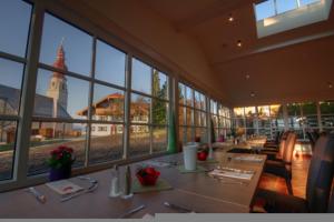 ein großes Zimmer mit Tischen und Fenstern mit einem Uhrturm in der Unterkunft Hotel Kirchbichl in Hallwang