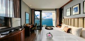 a bedroom with a bed and a desk with a view of the ocean at Boton Blue Hotel & Spa in Nha Trang