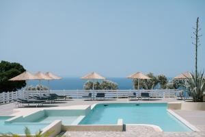 a swimming pool with chairs and umbrellas and the ocean at Mandilada Family Village - Seaview Villas in Marathokampos