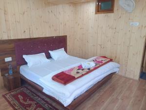 a bedroom with a bed with white sheets and wooden walls at Hotel Cafeteria Roof in Kalpa