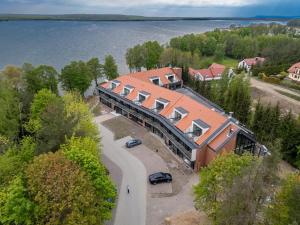 a building with a red roof next to a lake at Blue & Green Masurian Hotel in Węgorzewo