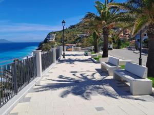 a sidewalk with benches and palm trees next to the ocean at Medoro Gioiosa 2 in Gioiosa Marea