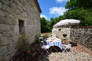 a table and chairs under an umbrella next to a stone wall at Maison en pierre à Laroque-Timbaut - Clévacances 3 clés in Laroque-Timbaut