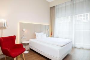 a bedroom with a white bed and a red chair at NH Collection Berlin Mitte Friedrichstrasse in Berlin