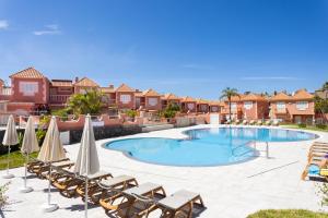 a swimming pool with chairs and umbrellas at Two modern and bright apartments near el Duque beach in Adeje