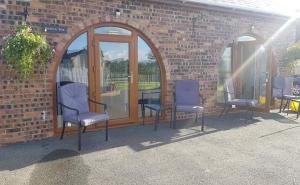 three chairs sitting in front of a brick building at Bwthyn Eira in Anglesey