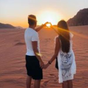 a man and woman standing in the desert watching the sunset at وادي رم in Wadi Rum