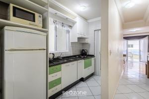a kitchen with white cabinets and a microwave at Aptos completos a passos do mar em Meia Praia – OBS in Perequê