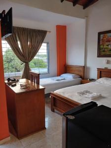 a bedroom with two beds and a desk and a window at Hotel El Descanso Montelíbano in Montelíbano