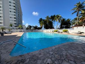 a blue swimming pool with palm trees and a building at Downtown Isla Verde Beachfront Apartment with Pool and Parking in San Juan