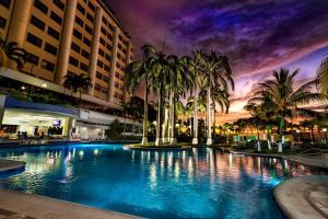a large swimming pool with palm trees and buildings at Hotel Olé Caribe in Macuto