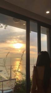 une femme assise devant une fenêtre regardant le coucher du soleil dans l'établissement Khách sạn IBIZA Hải Tiến - Căn hộ IB15A06 Premier Ocean, à Nam Khê