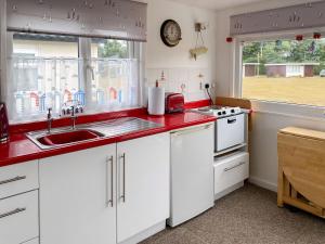 a kitchen with white cabinets and a red counter top at Driftwood in Mundesley