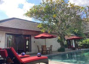 ein Haus mit einem Pool, Stühlen und einem Sonnenschirm in der Unterkunft Enchanting Canggu Villa in Tumbak Bayuh