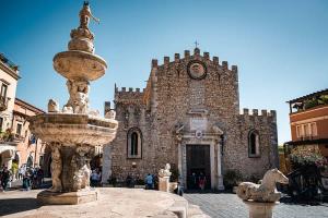 una fontana di fronte a un edificio con torre dell'orologio di Holiday Room "Pomelia 2" Taormina a Taormina