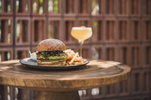 a sandwich and french fries on a plate with a glass of wine at Blossom Eco Luxe Villas by Ekosistem in Canggu