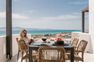 a woman sitting at a table on a balcony at Lithia Exclusive Villas & Suites in Plaka