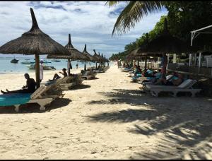a group of people sitting on a beach with straw umbrellas at Grand Baie la Croisette villa du bonheur Chez Marie in Hermitage