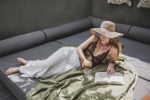 a woman in a hat laying on a bed with a book at Blossom Eco Luxe Villas by Ekosistem in Canggu