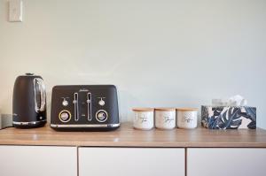 a toaster and three coffee cups on a counter at Brand New Guest House in Kenmure Dunedin in Dunedin