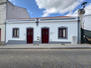 a white building with red doors on a street at Casas do Mercado, 3 in Montemor-o-Novo