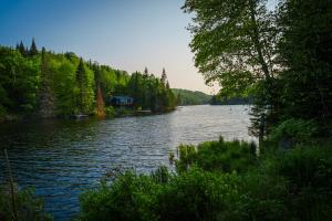 a view of a lake with a house on the shore at Le Chalet Brun, jacuzzi en bord de lac in Saint Adolphe D'Howard