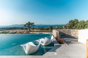 a swimming pool with two white chairs sitting next to the water at Akres Luxury Sea View Villas in Psalidi +41 photos