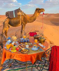 a table with food and a camel in the desert at Merzouga heritage camp in Merzouga