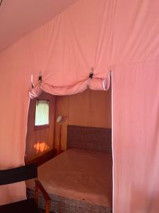 Una cama en una tienda de campaña rosa con ventana. en Tente Lodge en pleine nature, en Cros