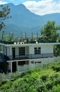 una casa blanca con una valla y montañas al fondo en White House Resort, en Balangoda