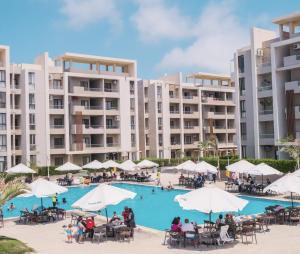 an image of a resort pool with tables and umbrellas at شاليه عائلي في قرية جراند هيلز طابق أرضي بحديقة خاصة غرفتين نوم وريسبشن واسع in Dawwār ‘Abd Allāh