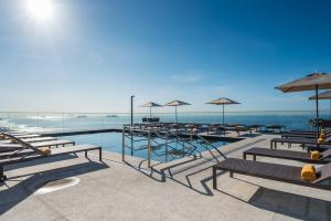 a swimming pool with benches and umbrellas and the ocean at Windsor Marapendi Hotel in Rio de Janeiro