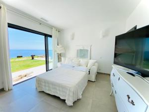 a white bedroom with a bed and a large window at Villa prestige au bord de l'eau- Pietracorbara in Pietracorbara