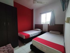 two beds in a room with red walls and a window at Hotel Madeleine Inn Sede Sur in Barranquilla