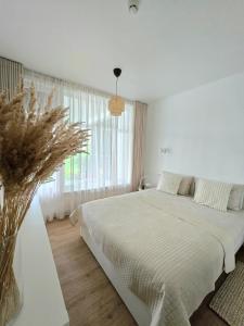 ein weißes Schlafzimmer mit einem Bett und einer Vase aus Blumen in der Unterkunft Haustory Palanga Apartment in Palanga