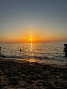 una puesta de sol en la playa con gente en el agua en Oro Verde, en Sedini 4 fotos más