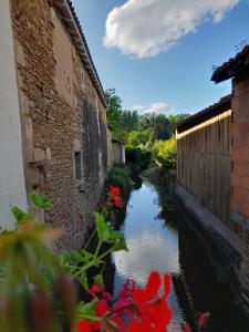a small canal next to a building with red flowers at Gîte de baigneux 2 étoiles in Moncontour-de-Poitou