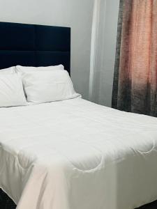 a bed with white sheets and a blue headboard at Grey Vacation Home in Gaborone