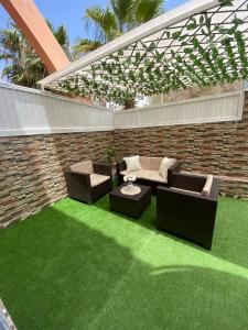 une terrasse avec de l'herbe verte, un canapé et des chaises dans l'établissement Appartement avec terrasse - séjour détente à quelques pas de la plage, à Agadir nʼ Aït Sa