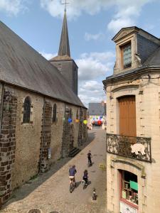 three people riding bikes down a street next to a church at Beaumont Vélo le Gîte in Beaumont-sur-Sarthe
