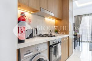 Bloomfields Deluxe Studio In Azizi Riviera في دبي: مطبخ مع موقد وغسالة ومجفف