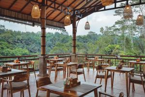 a restaurant with tables and chairs and a view of the forest at Harsa Sanctuary by GenuineHost in Ubud