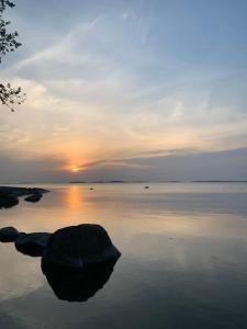 a sunset over a body of water with a rock in the water at Omakotitalo veistämöllä meren rannassa in Hanko +3 photos