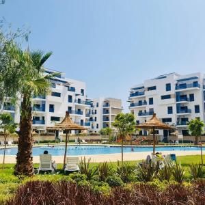 a swimming pool with chairs and umbrellas and buildings at Ground floor apartment,facing swimming pool, wifi , air conditioner in Martil